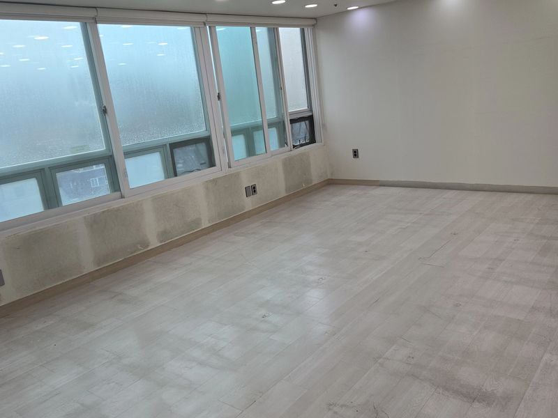 천장 냉난방기와 조명이 남아있고 벽 하단 마감재가 제거된 교습소 내부